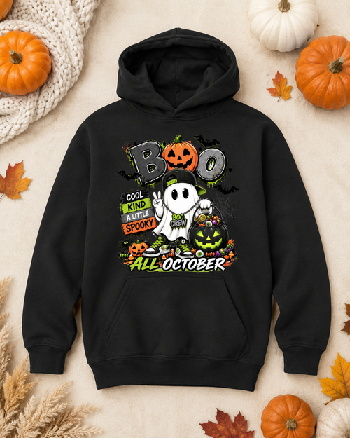 A black pullover hoodie with a colorful Halloween graphic on the chest, displayed in a flat-lay arrangement with pumpkins, autumn leaves, and a knitted blanket on a beige background.