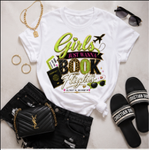 A white graphic T-shirt laid flat with black shorts, black Christian Dior slip-on shoes, a black quilted handbag, gold rings, sunglasses, and a gold necklace arranged around it on a white background. The shirt graphic reads 'Girls Just Want A BOOK Flight' in green, yellow, and black lettering.