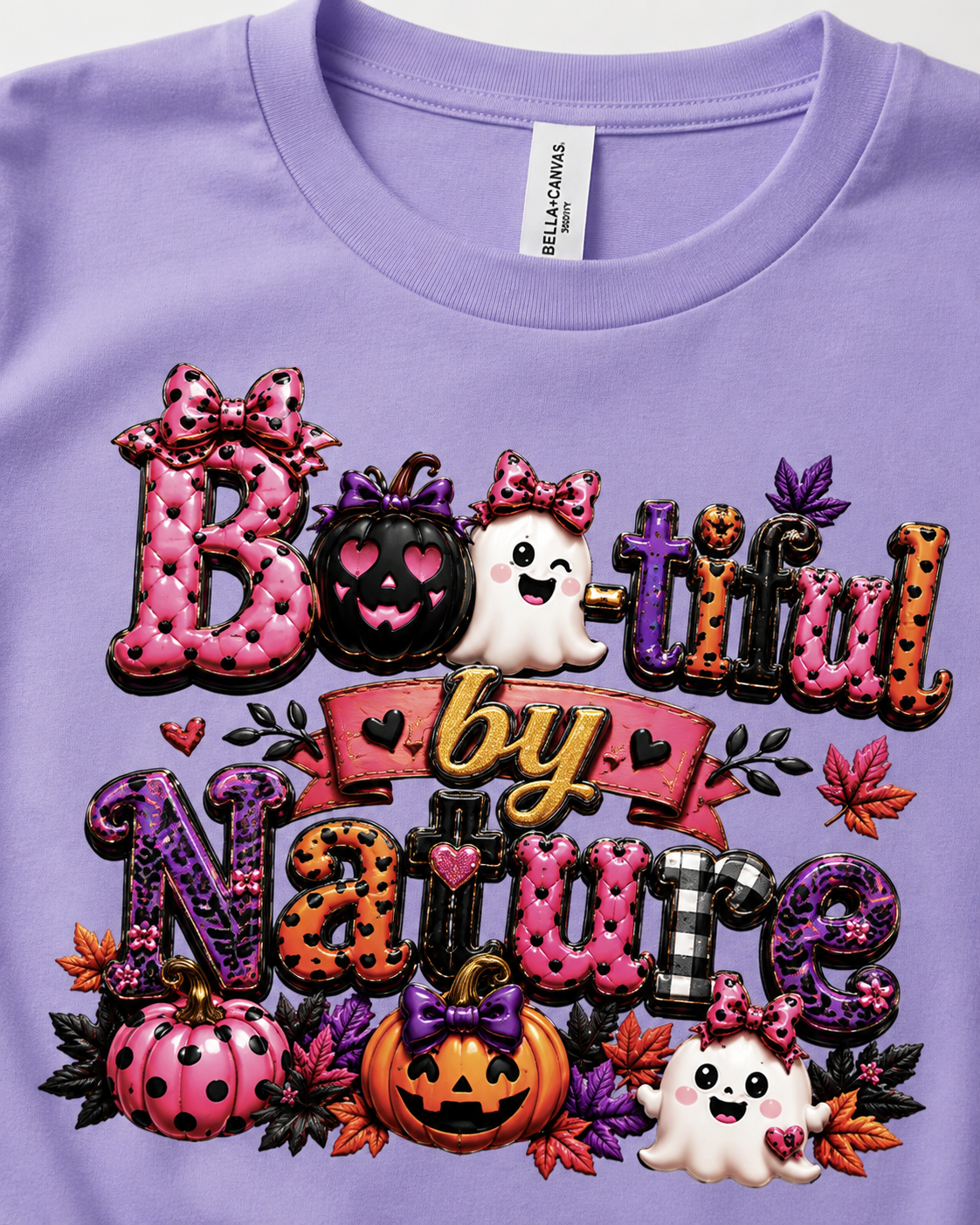 A close-up of a lavender Bella+Canvas t-shirt featuring a colorful, textured graphic that reads 'Boo-tiful by Nature' with Halloween motifs including pumpkins, ghosts, and autumn leaves.